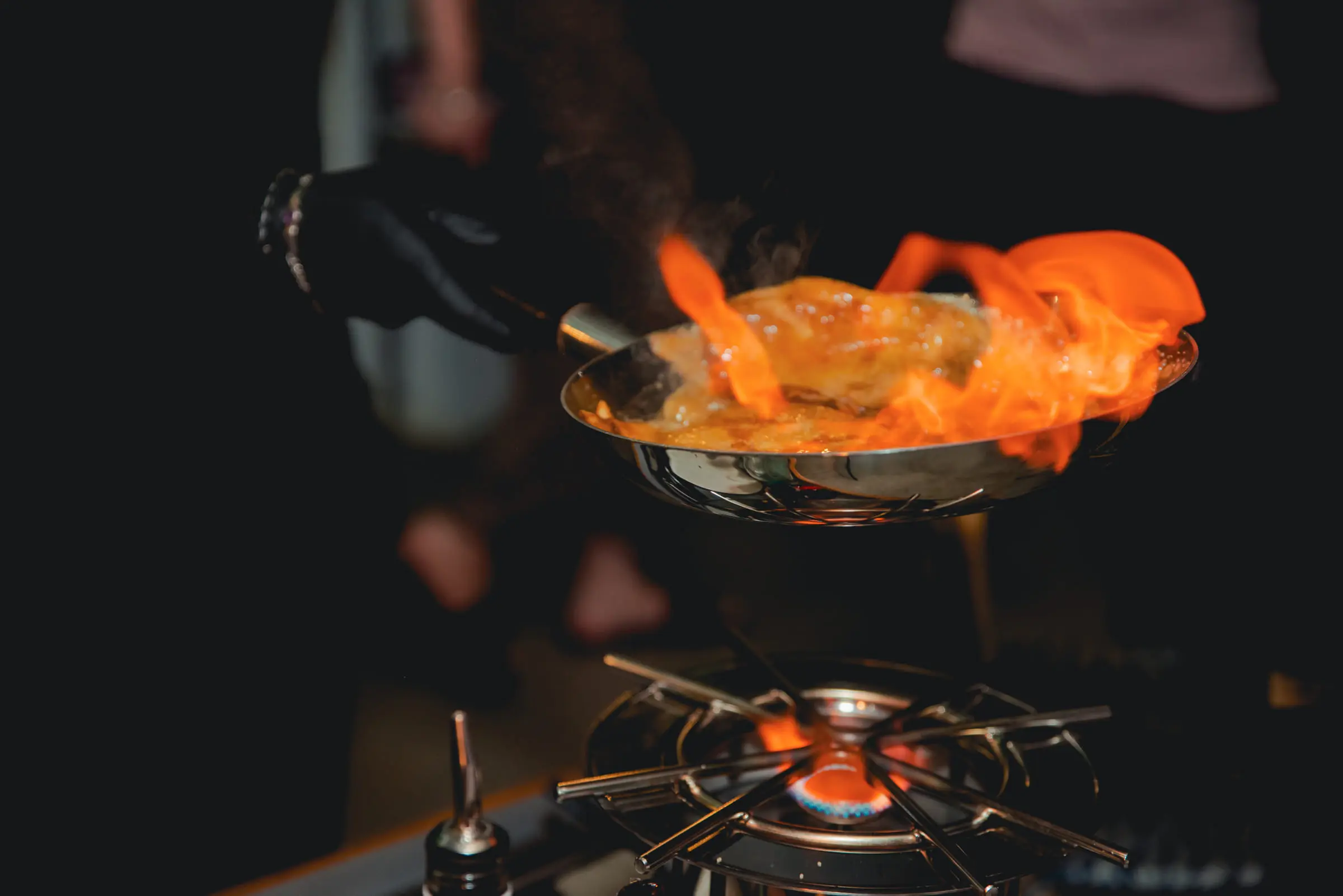 A chef finishing a dish in the flambé pan