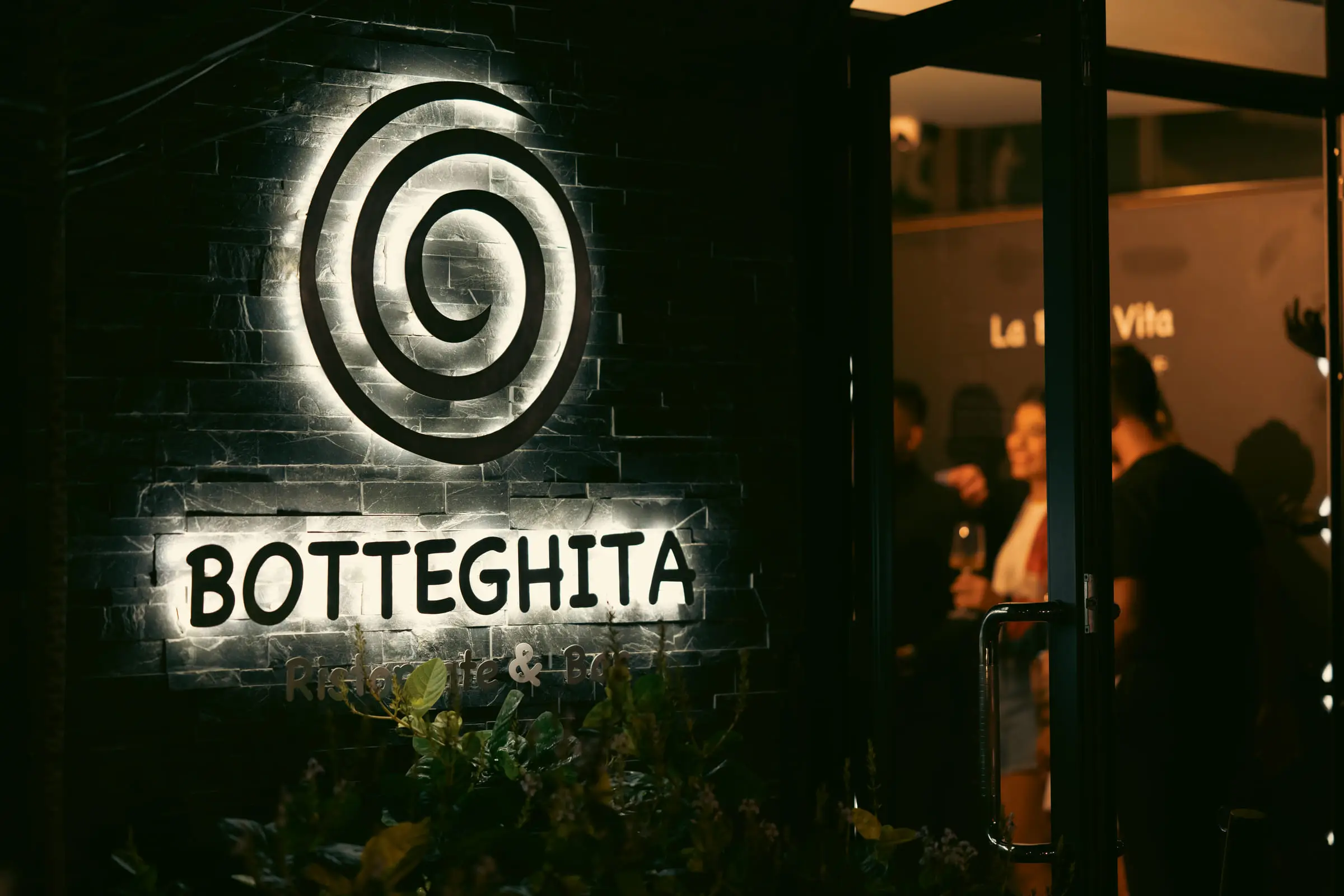 The illuminated Botteghita sign at the entrance on a Grand Baie evening
